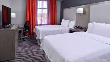 A hotel room with two beds, a desk, a chair, a TV, and a window with red curtains.