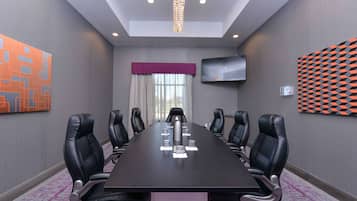 Un salón de conferencias con una larga mesa, sillas de cuero negro, un televisor de pantalla plana y una pared con diseño.