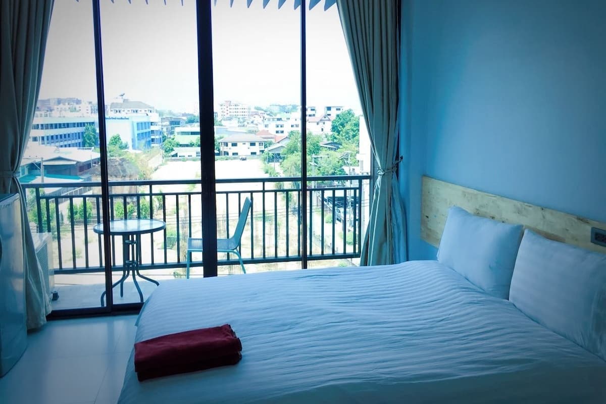 A hotel room with a large bed, a balcony with a table and chairs, and a view of the cityscape.