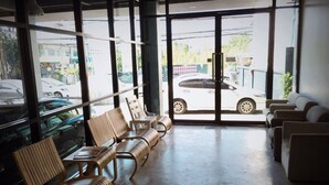 A waiting area with wicker chairs and sofas, large windows with a view of parked cars and buildings outside. - Sirin Loft Resident (Chiang Mai)
