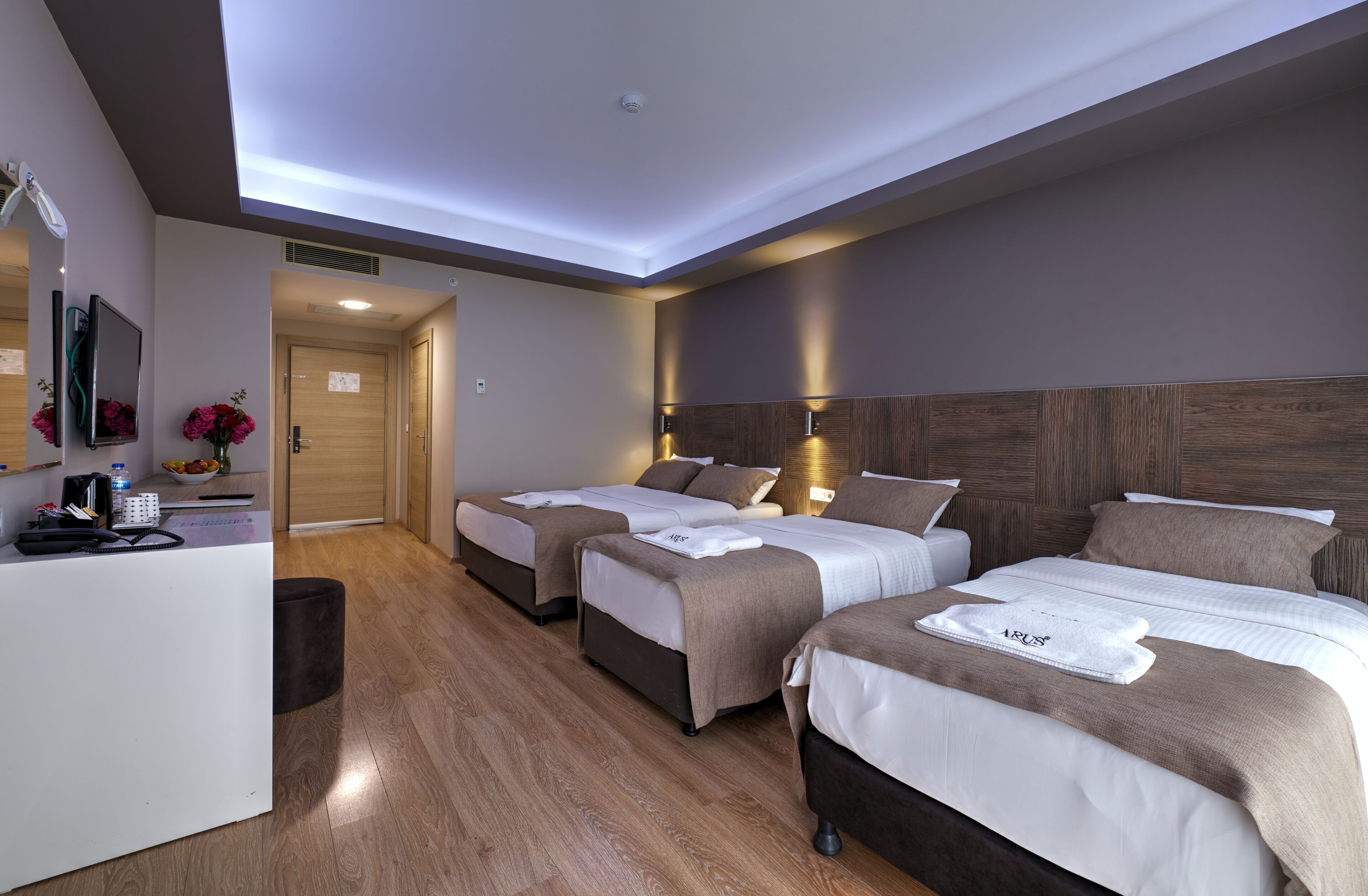 Ein Hotelzimmer mit drei Betten, einem Schreibtisch mit Computer und Telefon sowie einem kleinen Badebereich.