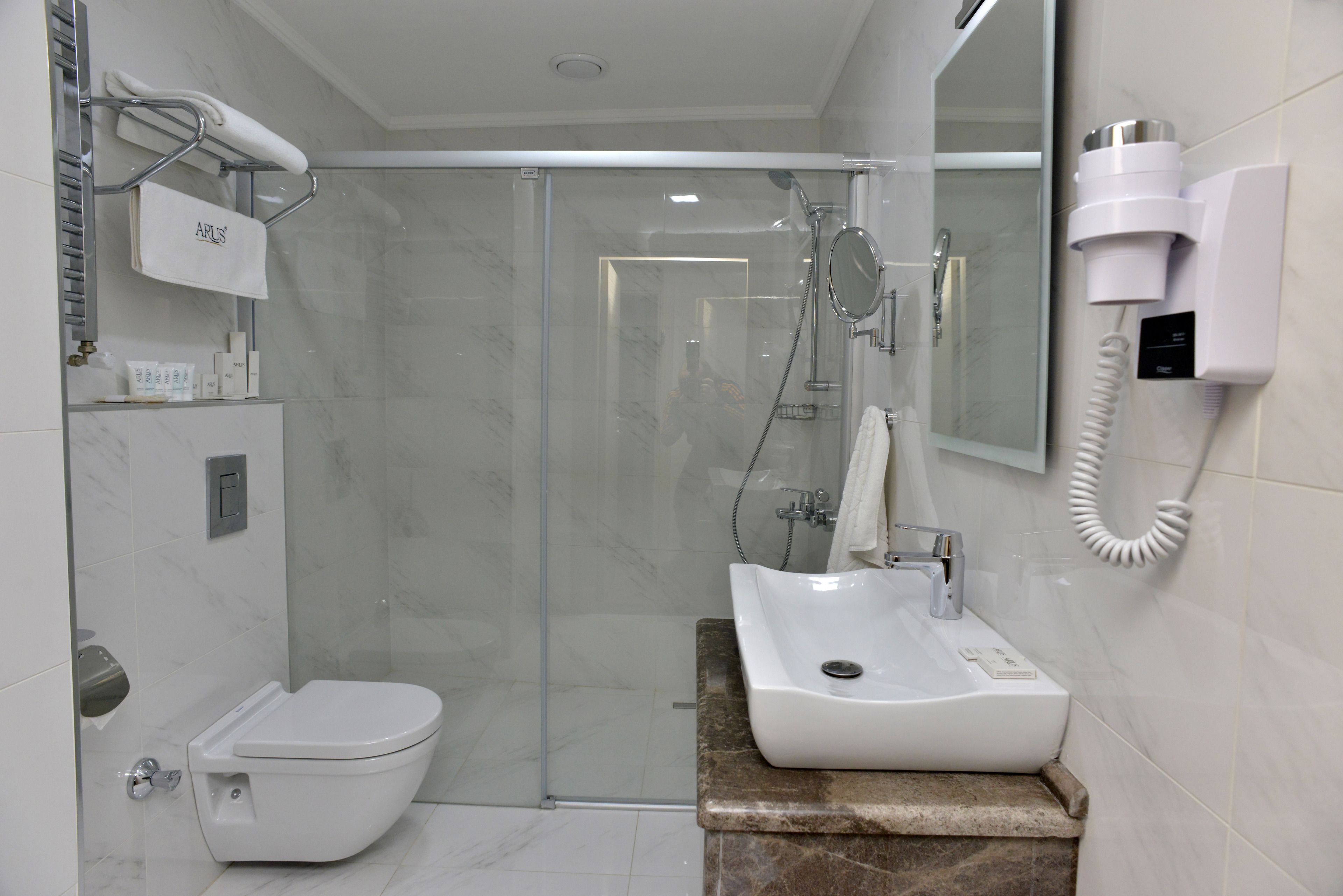 Une salle de bain moderne équipée de toilettes, d’un lavabo, d’une douche à parois de verre et d’un sèche-cheveux fixé au mur.