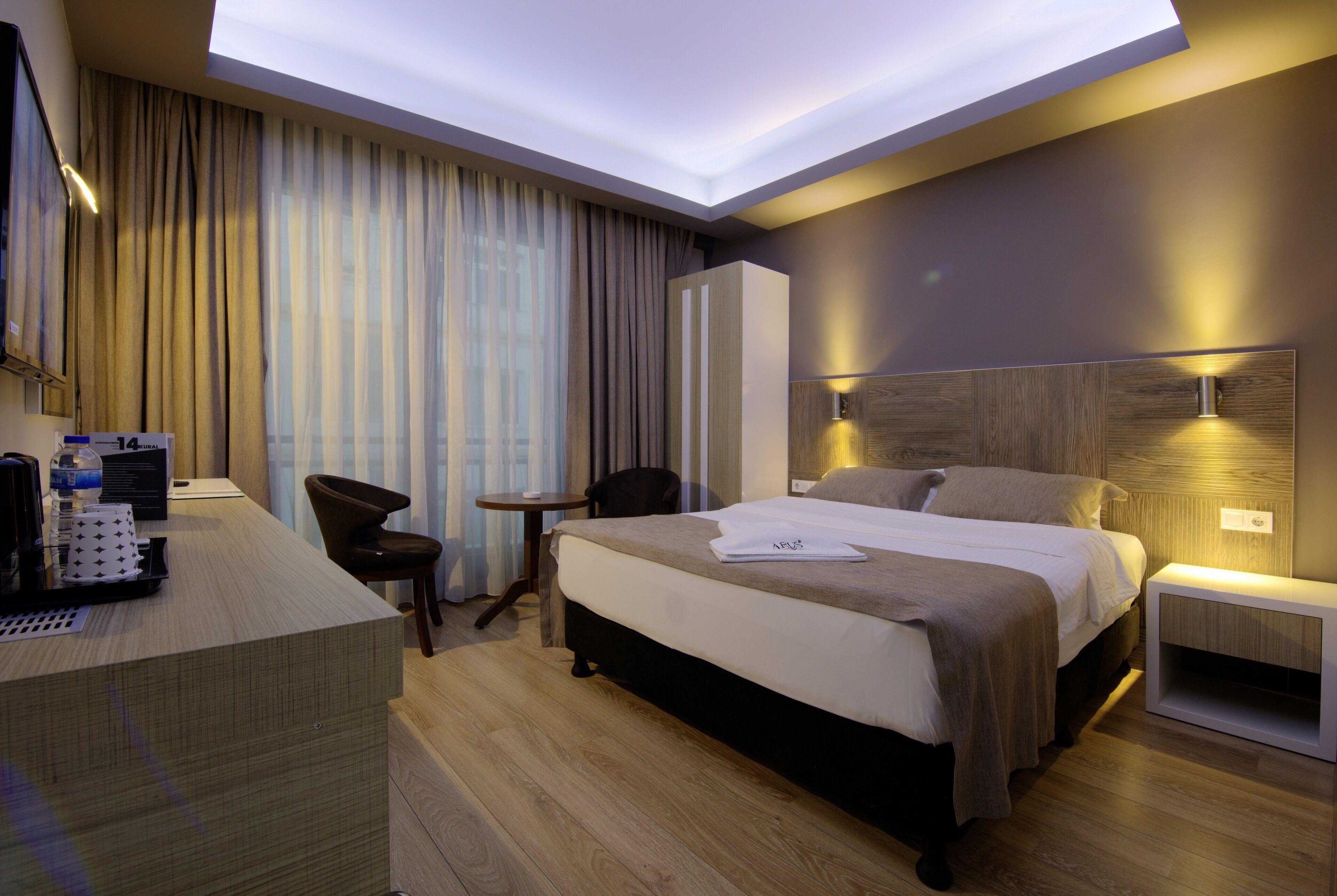 Una habitación de hotel moderna con una cama grande, un escritorio, una silla, una mesita pequeña y una mesita de noche.