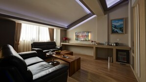A modern living room with a sofa, coffee table, and a kitchen area with a fridge and microwave. - Arus Hotel (Eskisehir)