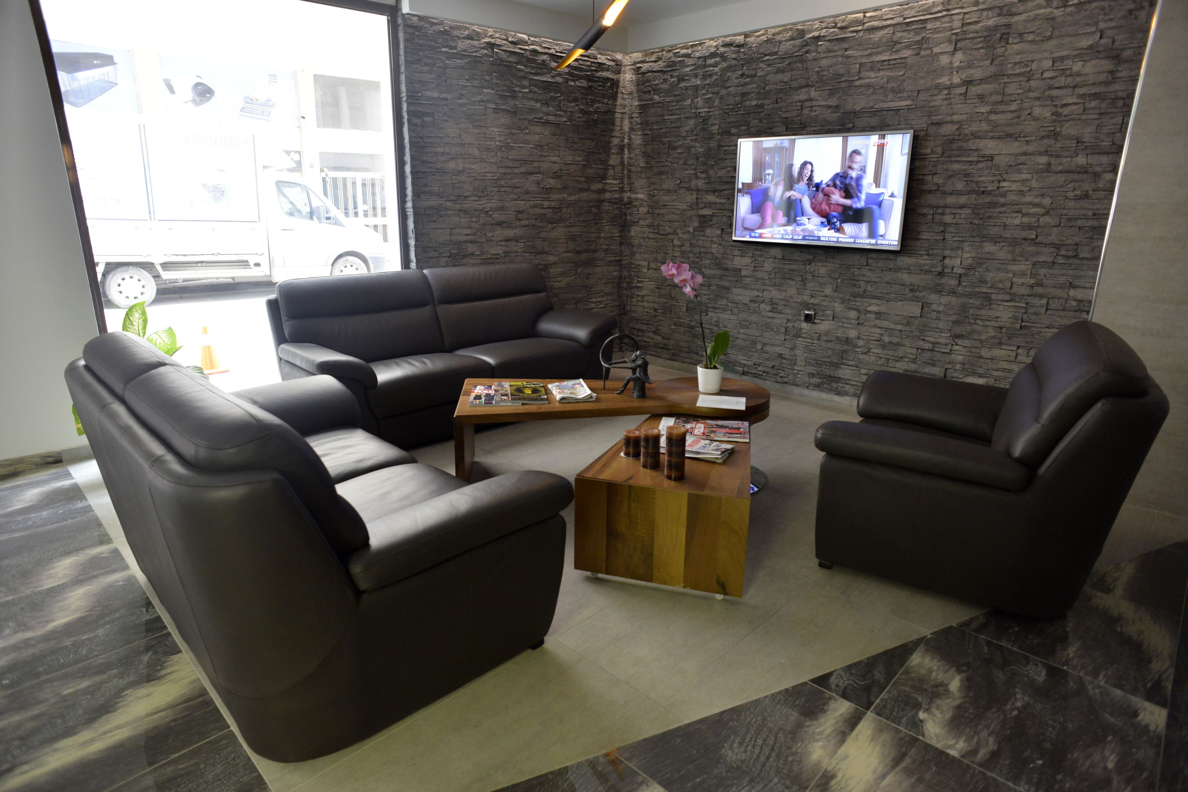 A modern living room with a black leather sofa, a wooden coffee table, and a TV mounted on a brick wall.