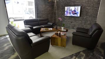 A modern living room with a black leather sofa, a wooden coffee table, and a TV mounted on a brick wall.