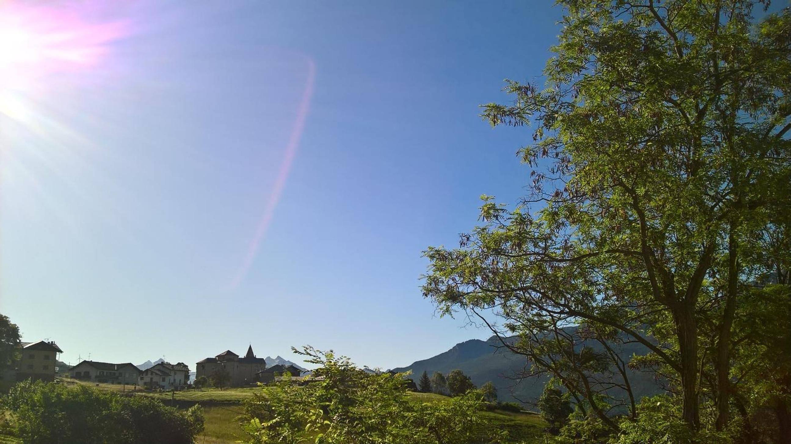 A rural landscape with houses, a clear sky, and mountains in the background.