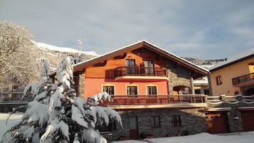 A multi-story building with a balcony, stone lower level, and snow-covered surroundings.