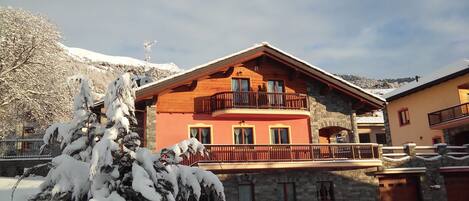 A multi-story building with a balcony, stone lower level, and snow-covered surroundings.