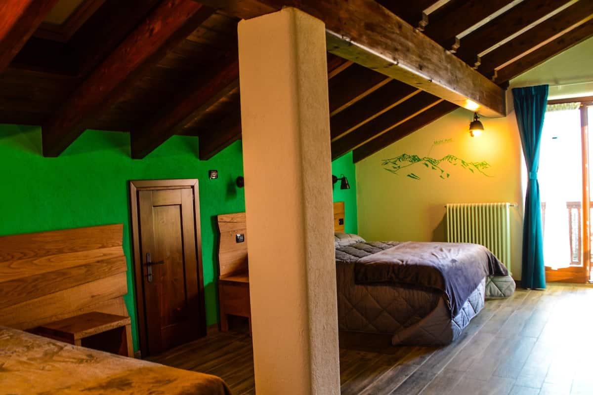 A room with a wooden ceiling, a bed with a quilted cover, a wooden bench, a door, and a radiator.