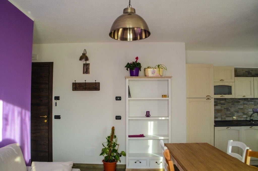 Una cocina compacta con armarios blancos, encimera de madera y una lámpara colgante.