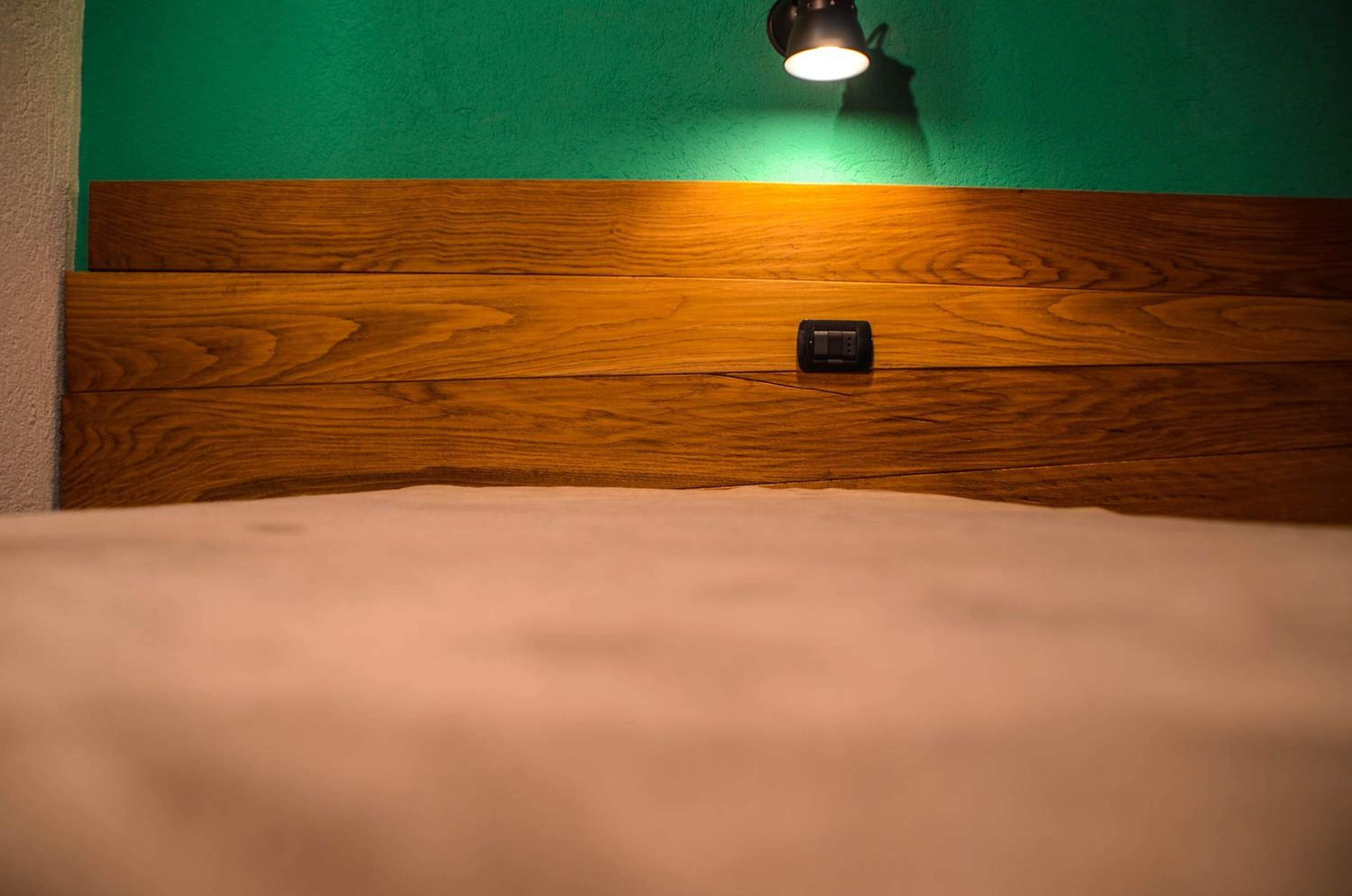 Un letto con testiera in legno e una lampada fissata al muro.
