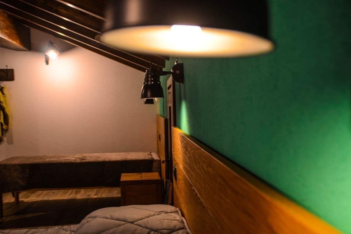 A small, cozy room with a wooden bench, a single bed, and a wall-mounted lamp.