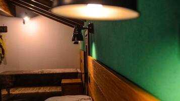 A small, cozy room with a wooden bench, a single bed, and a wall-mounted lamp.