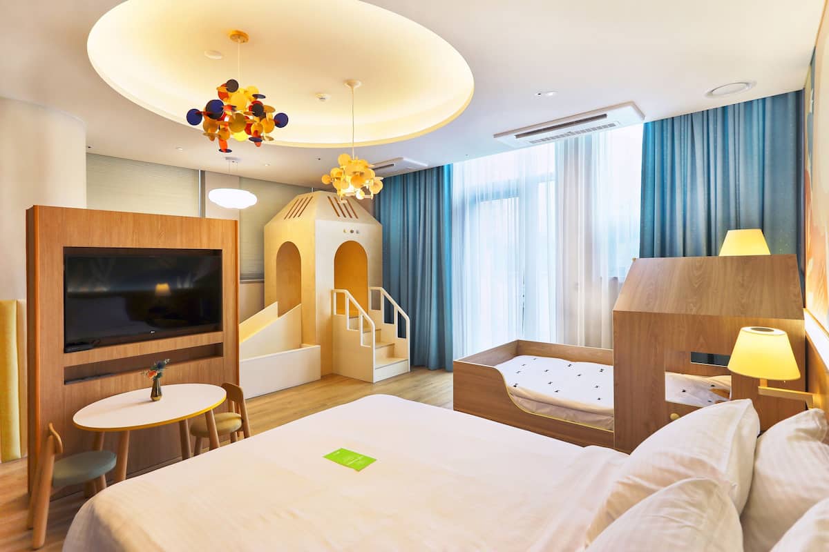 A hotel room with a bed, a TV, a small table with chairs, a lamp, and a staircase leading to a loft area.