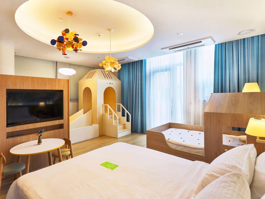 Quarto de hotel com cama, televisão, mesa pequena com cadeiras, luminária e escada que leva a um mezanino.