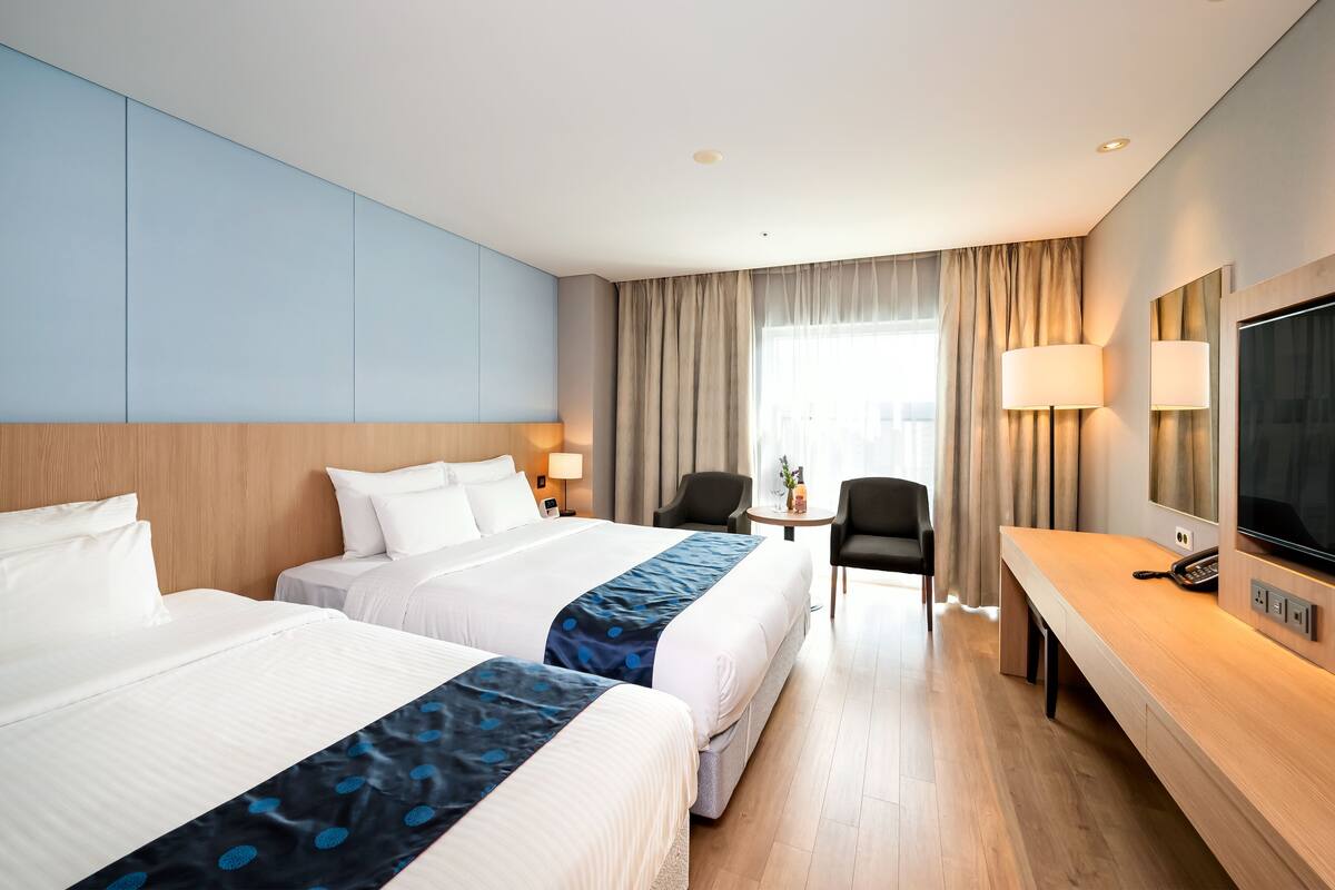A hotel room with two beds, a desk with a TV, and a small table with chairs.