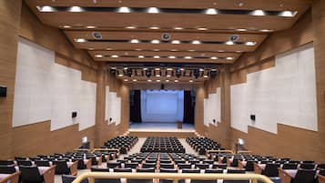 Ein modernes Auditorium mit terrassenförmigen Sitzreihen, Holzvertäfelung und einer großen Leinwand im vorderen Bereich.
