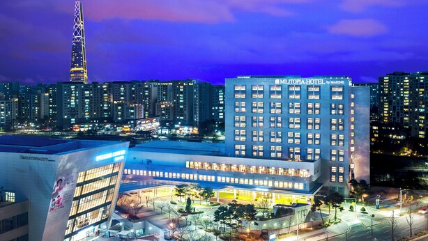 A modern hotel with a prominent sign, surrounded by high-rise buildings and a tall tower in the background. - Wirye Militopiahotel By Marine (Seongnam)