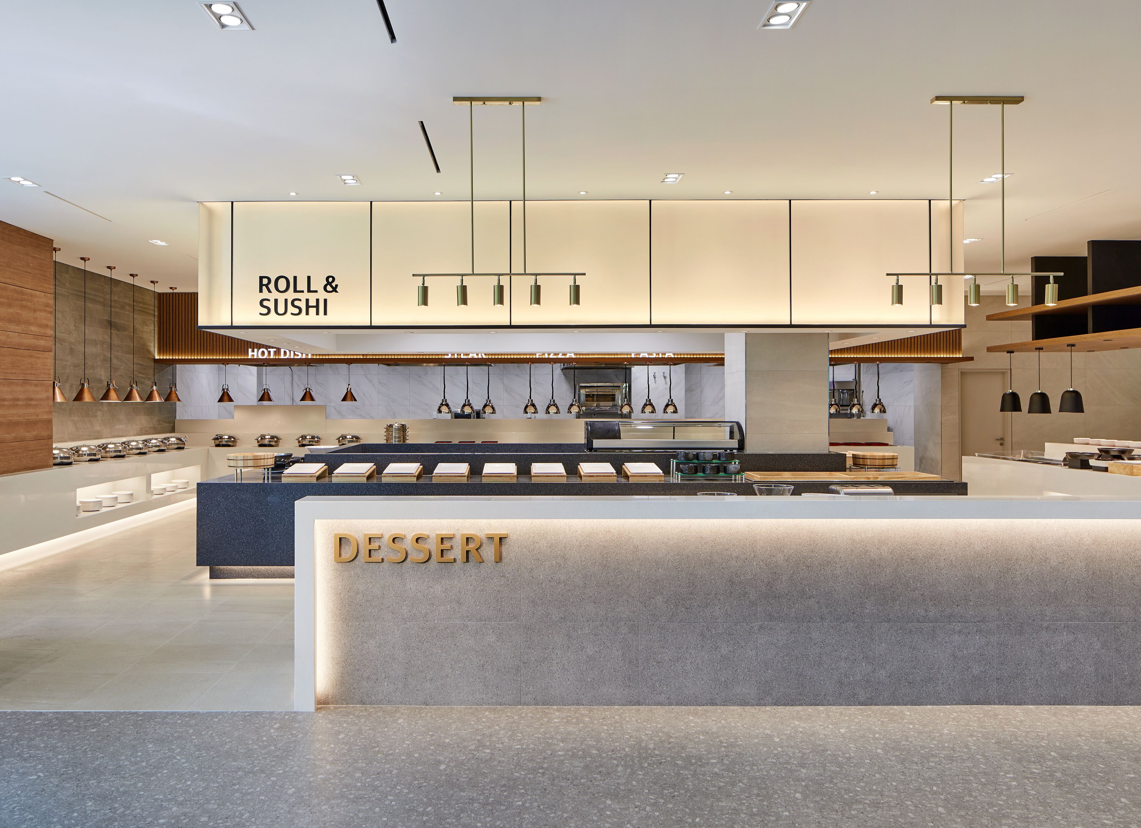 Un interior de restaurante moderno con barra de sushi, mostrador de postres e iluminación contemporánea.