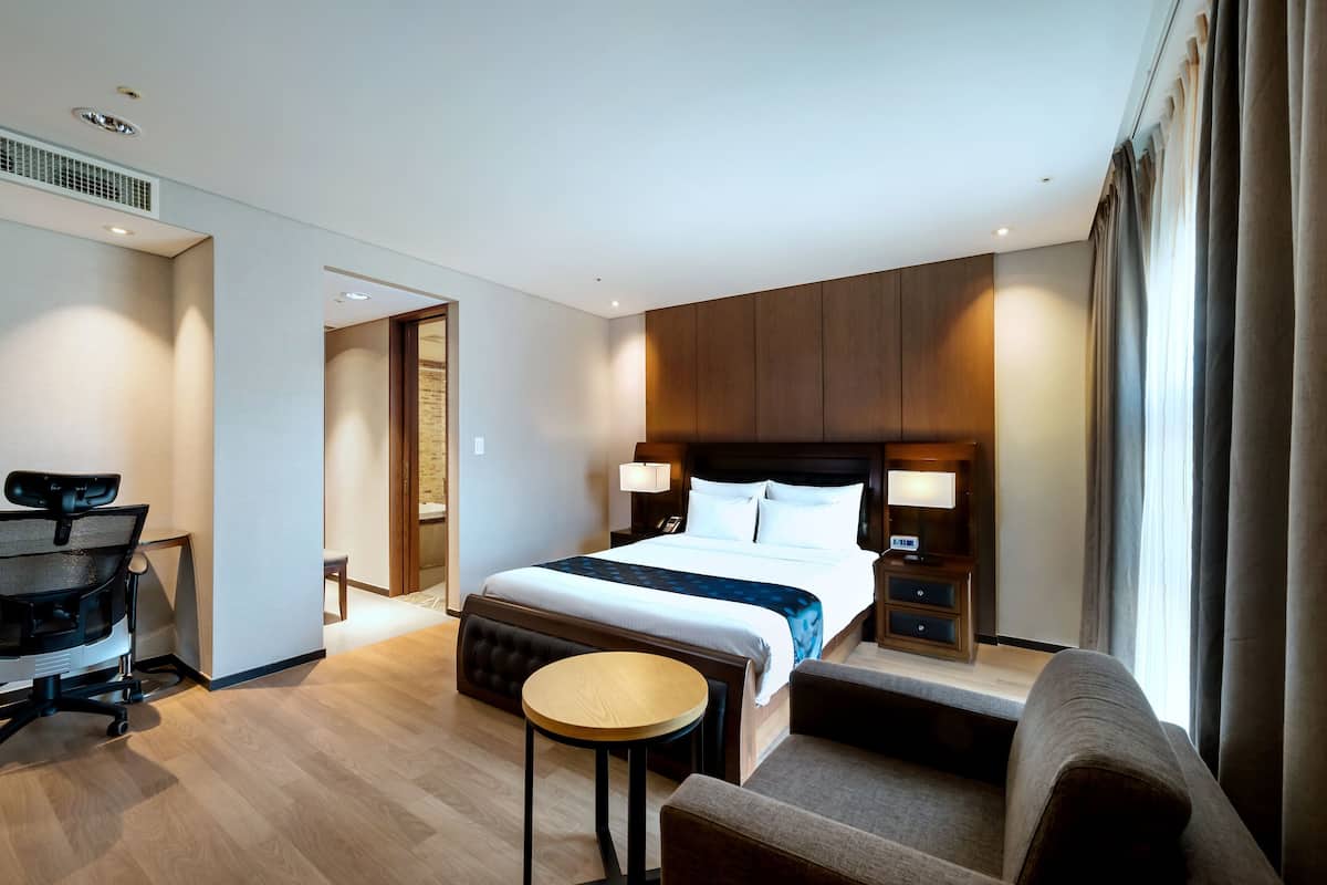 A modern hotel room with a large bed, bedside tables, a desk, and a chair.