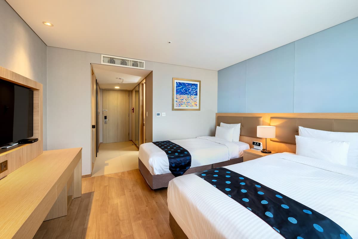 A hotel room with two beds, a desk, a TV, and a painting on the wall.