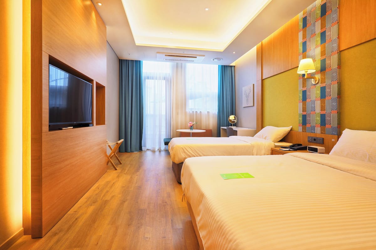 A hotel room with two beds, a flat-screen TV, a small table, and a desk with a lamp.