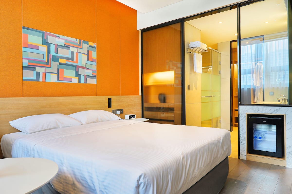 A modern hotel room with a large bed, a small table, a glass shower area, and a unique wall art piece.