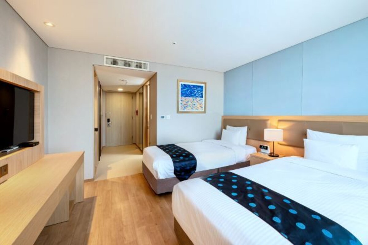 Una habitación de hotel con dos camas, televisión, escritorio y un cuadro en la pared.