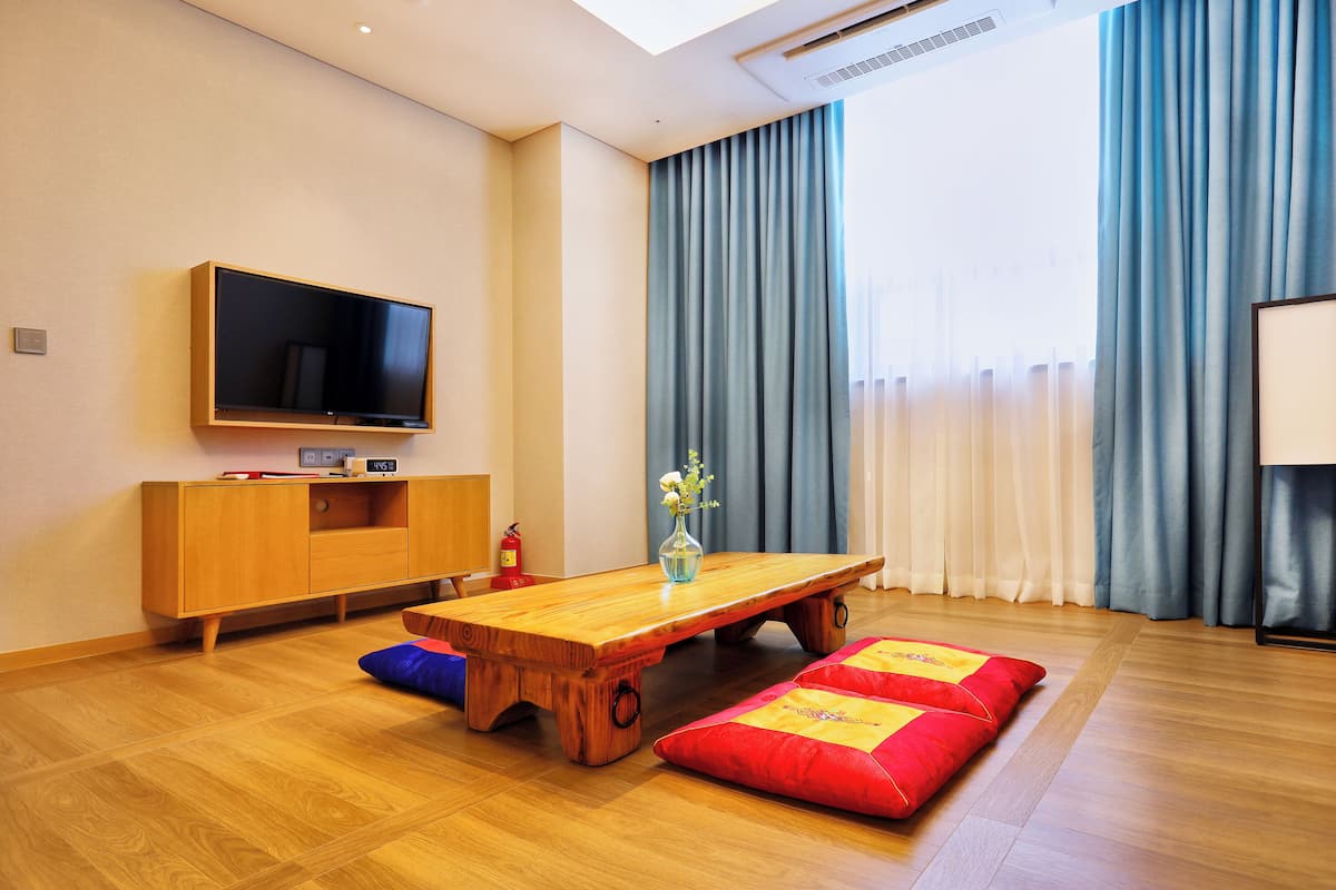 A modern living room with a wooden coffee table, red and yellow cushions, a flat-screen TV, a wooden cabinet, and a vase with flowers.
