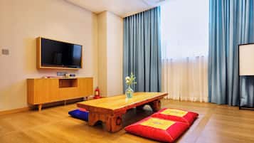A modern living room with a wooden coffee table, red and yellow cushions, a flat-screen TV, a wooden cabinet, and a vase with flowers.