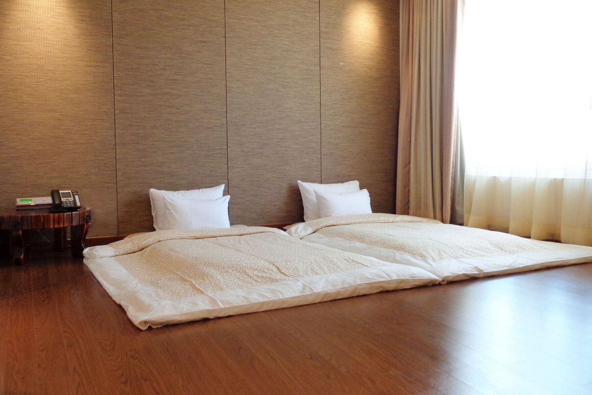 A hotel room with a large bed, a bedside table with a phone, and a window with curtains.