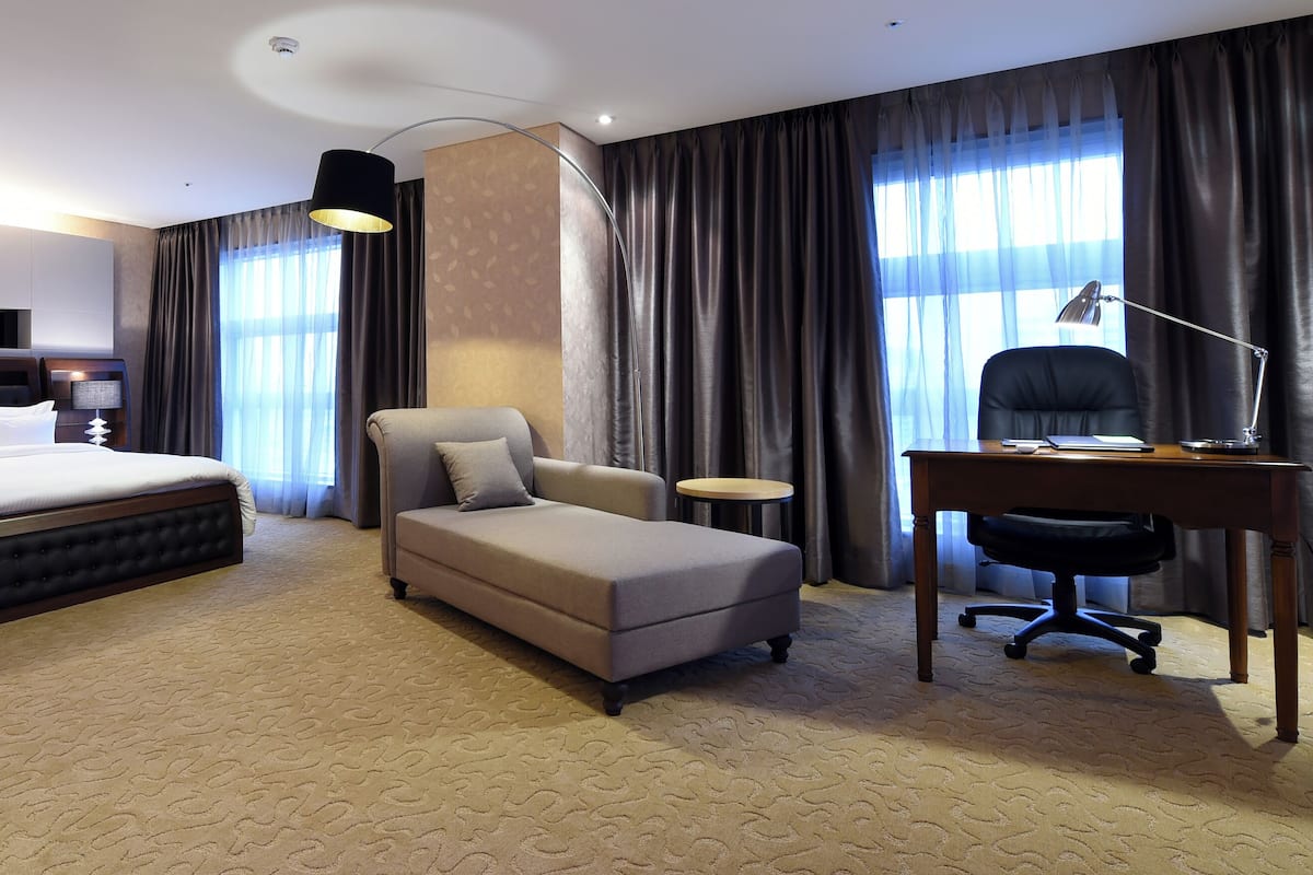 A hotel room with a large bed, a sofa, a desk, and a chair.