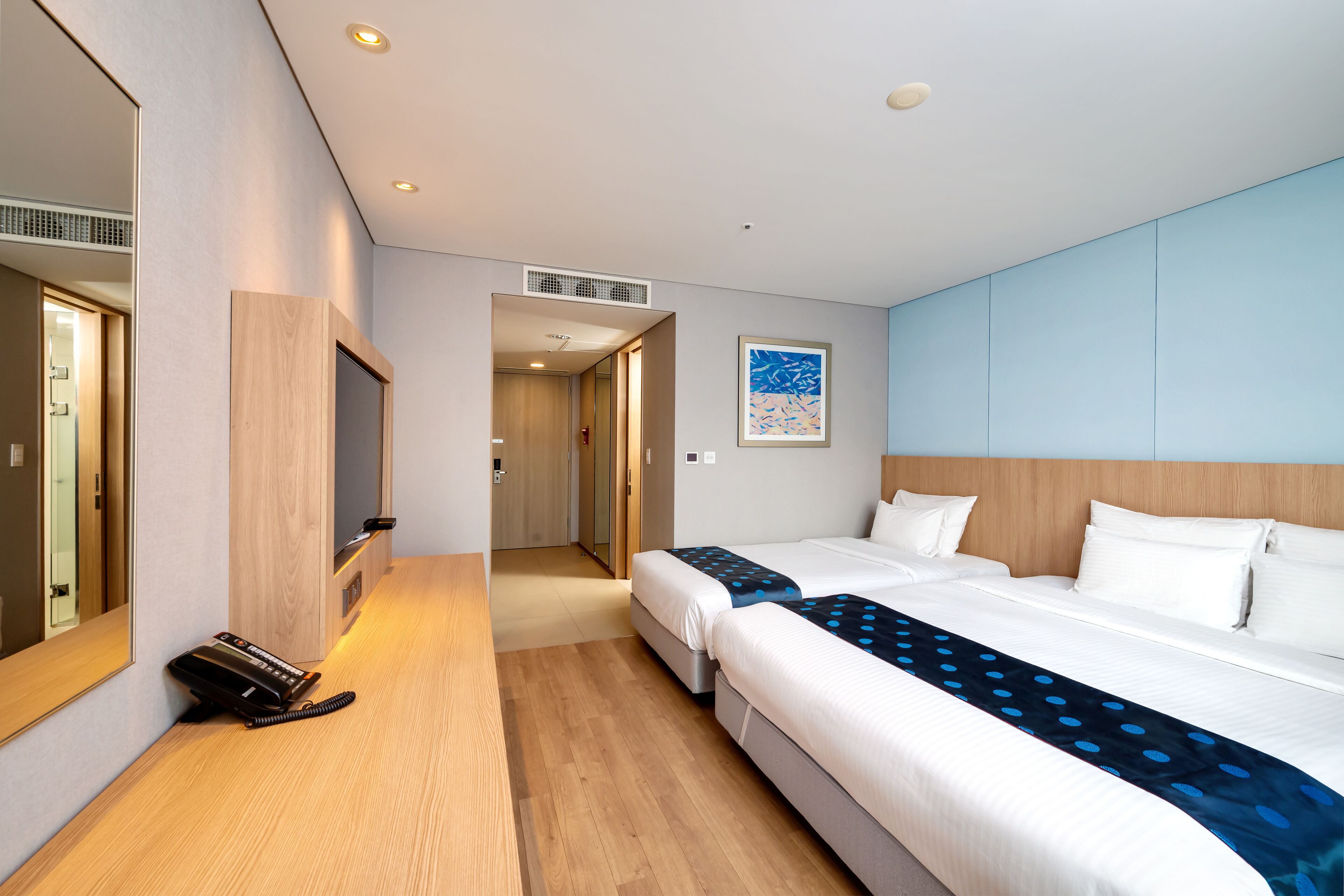 A hotel room with a large bed, a bedside table, a mirror, and a door leading to a hallway.