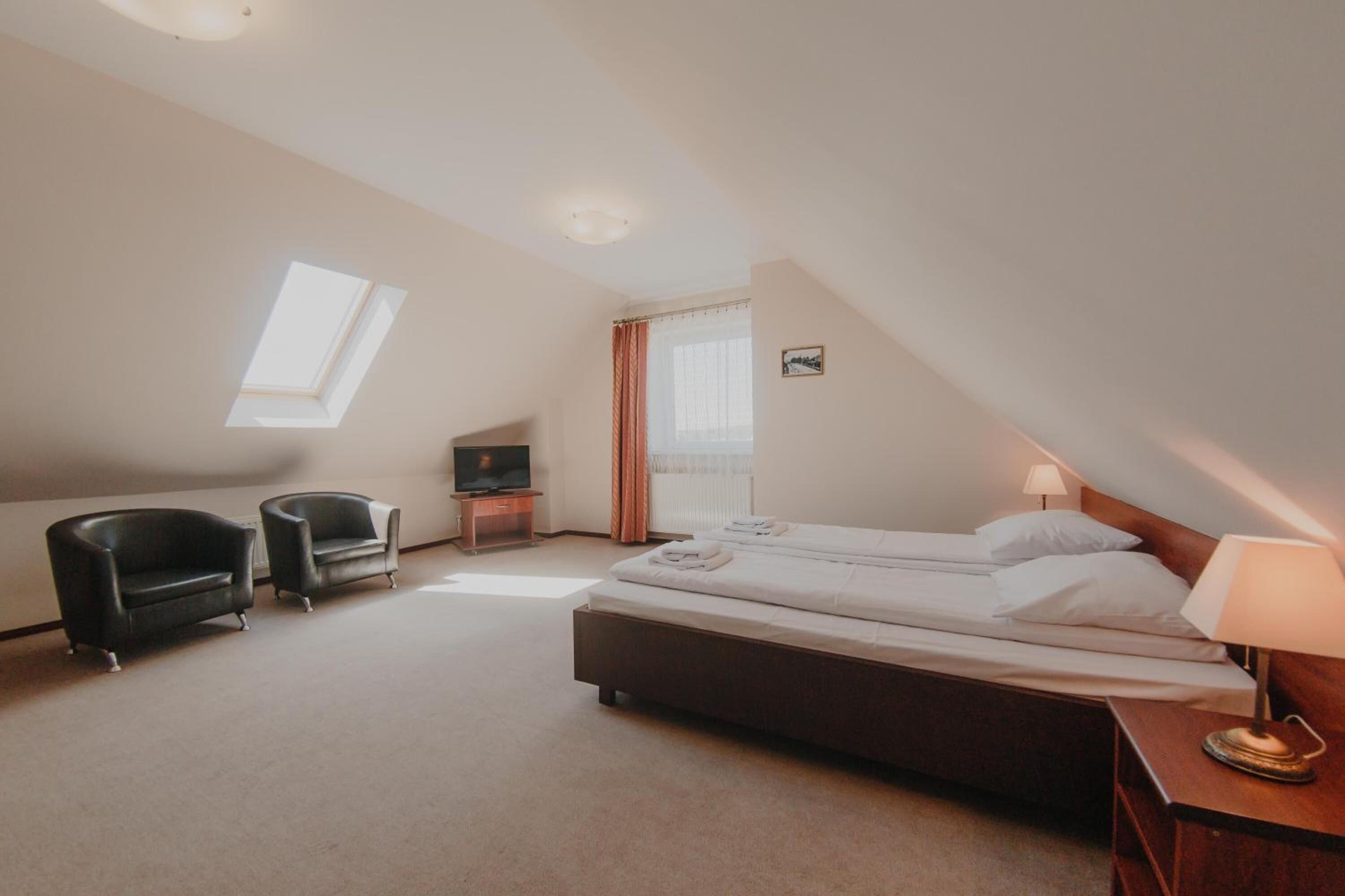 Une chambre d’hôtel avec un lit, deux fauteuils, une télévision, une fenêtre et une lampe.