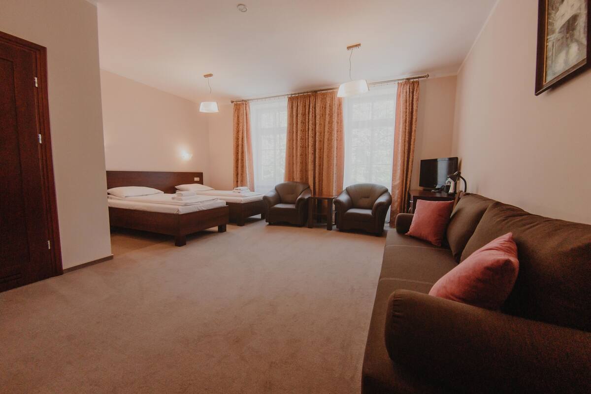 A hotel room with a bed, two armchairs, a sofa, a TV, and a painting on the wall.