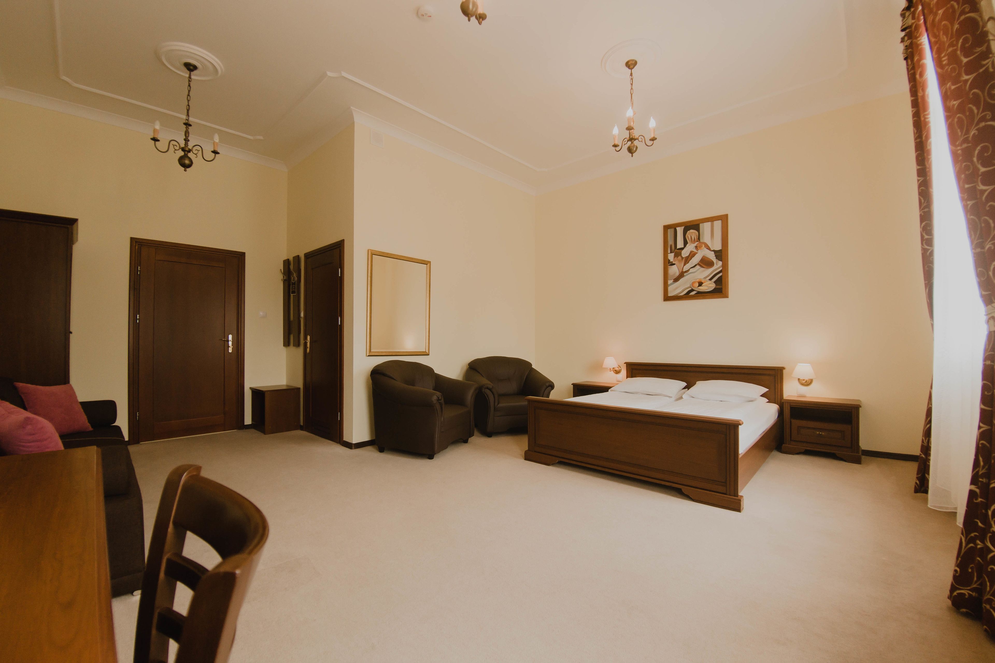 Une chambre d’hôtel avec un grand lit, deux tables de chevet avec des lampes, une chaise, un bureau et une porte.