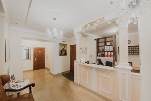 A reception area with a reception desk, a chandelier, and a framed portrait on the wall. - Hotel Cesarski (Gizycko)