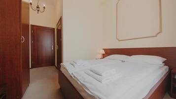 A bedroom with a wooden bed, white linens, a bedside table, a lamp, and a chandelier.