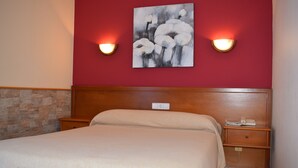 Habitación de hotel con cama, mesita de noche, un cuadro colgado en la pared y dos apliques.