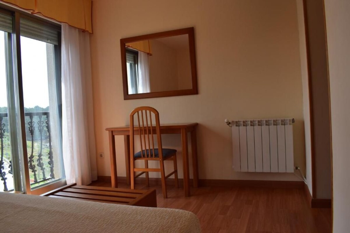 Een slaapkamer met een bed, een houten stoel, een kleine tafel, een spiegel en een radiator.