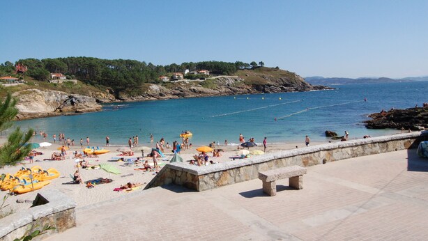 Una playa con gente, sombrillas y un muro de piedra.