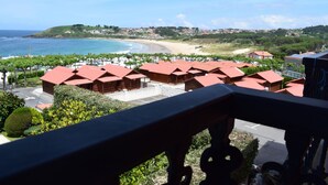 Un hotel costero con edificios de techo rojo, vista a la playa y un paisaje montañoso al fondo.