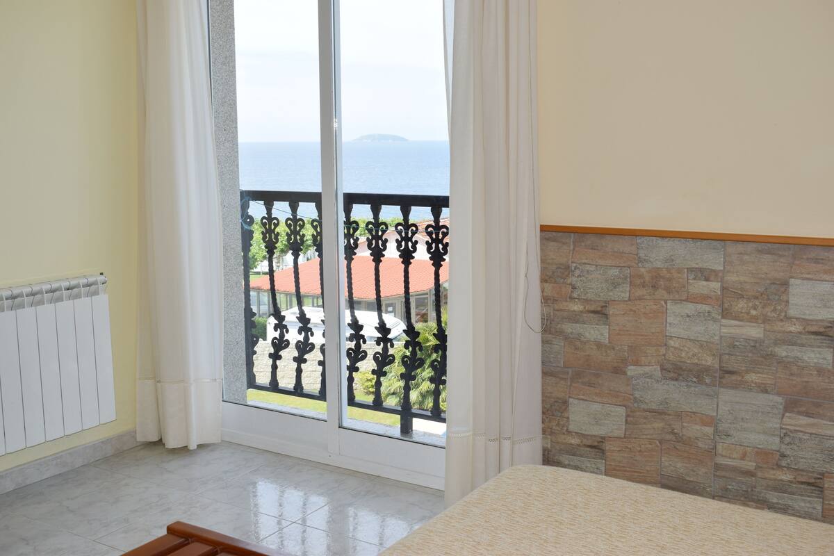 A room with a large sliding glass door leading to a balcony with a view of the sea.