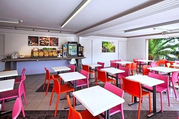 A restaurant with multiple tables and chairs, a counter with food items, and framed pictures on the wall.