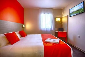 A hotel room with a bed, a desk, a TV, and a window with curtains.