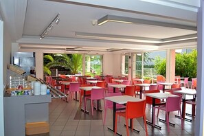 A restaurant with indoor seating, large windows, and a counter with beverages.