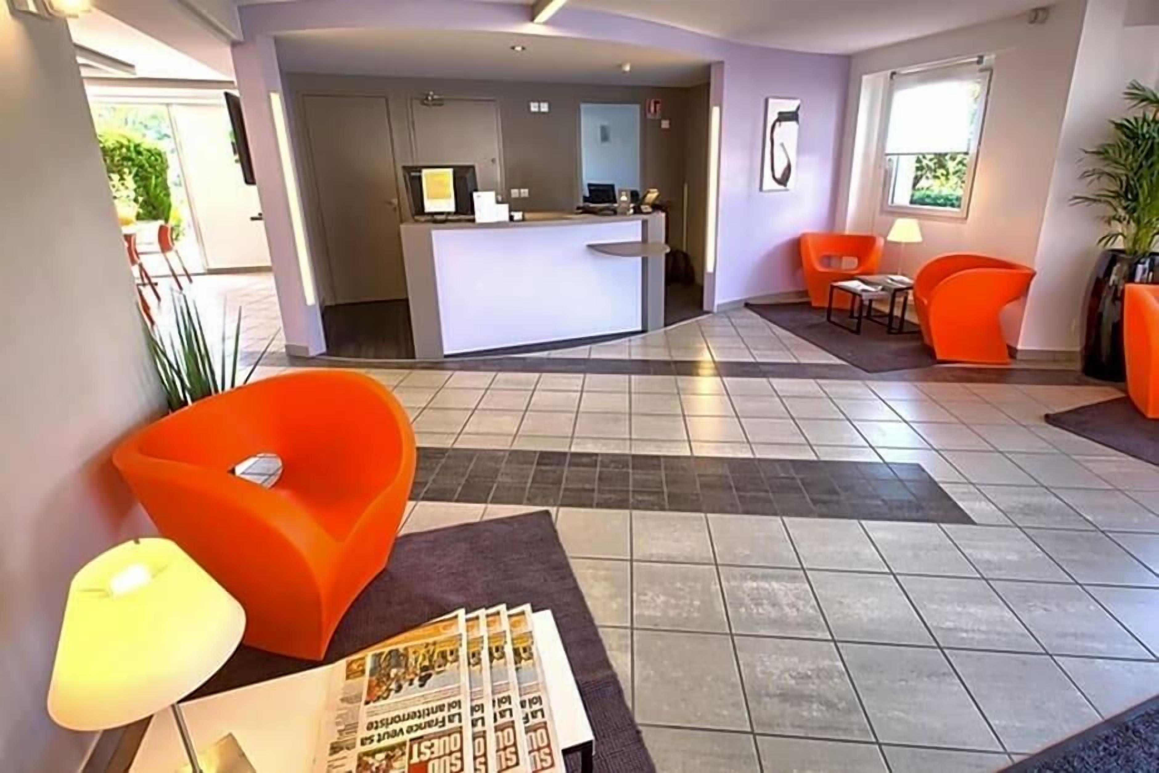 Eine moderne Hotellobby mit einer Rezeption, orangenen Sitzgelegenheiten und einem Fliesenboden.