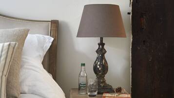 Een slaapkamer met een bed, nachtkastje met een lamp, een fles, een glas en een boek.