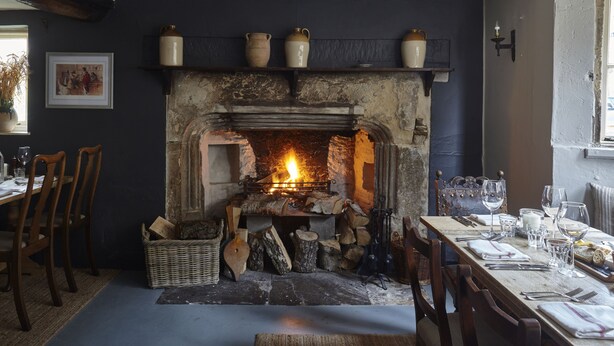 A cozy room with a fireplace, wooden chairs, a dining table set with glasses and cutlery, and a framed picture on the wall. - Sign of the Angel (Chippenham)